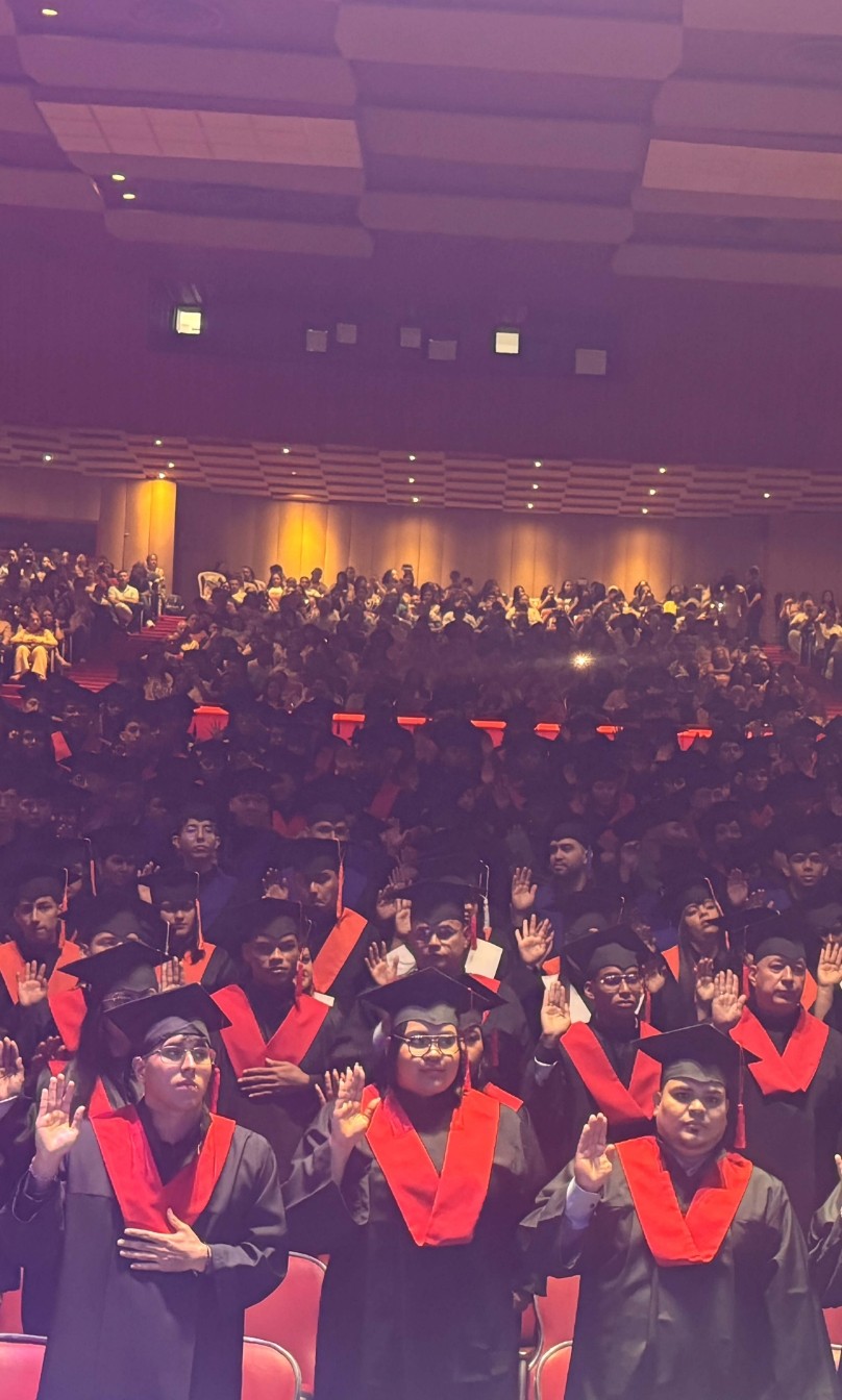 Ceremonia de graduación del PEC Politécnico Empresarial Colombiano, con estudiantes vestidos con toga y birrete levantando la mano durante el juramento profesional.