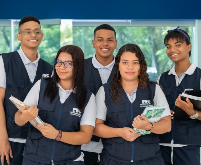 Estudiantes del Politécnico Empresarial Colombiano (PEC) con uniforme institucional, sonriendo y sosteniendo cuadernos en las instalaciones del campus.