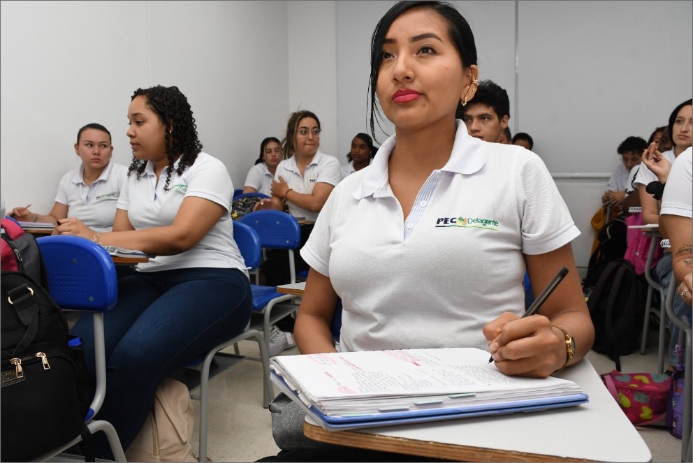 Estudiantes del Politécnico Empresarial Colombiano (PEC) participando en clase, con uniformes institucionales y tomando apuntes en el aula.